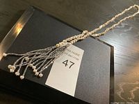 Full view of the necklace laid out on a black surface showing pearl chain and multiple beaded tassels with small pearls at ends.