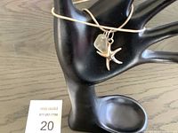 Necklace displayed on black jewelry hand stand showing chain and attached pendants including starfish and sea glass pendant.