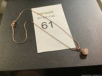 Full view of rose gold-tone necklace laid flat with pendant and chain visible, showing overall condition and design