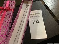 Silver chain necklace marked 925 displayed inside pink gift box with geometric patterns and a red ribbon bow.