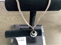 Photo of silver-tone chain necklace with circular pendant displayed on black holder