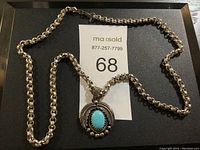 Full view of silver chain necklace with turquoise stone pendant on black surface with lot number.