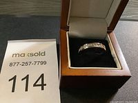 Silver-tone ring set with multiple clear stones on a black velvet cushion inside a brown and cream ring box.