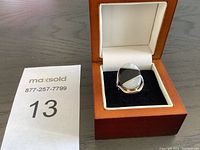 Ring inside a wooden box with white and black padded interior. The ring shows a black and white stone inlay on top, set in sterling silver.