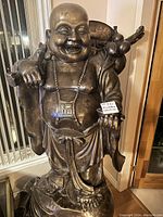 Front view of bronze-colored hollow metal Laughing Buddha statue on stand