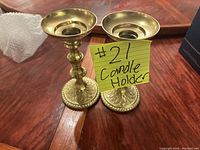 Pair of brass candle holders on a wooden table with a handwritten note 'candle holder #21'
