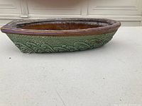 Side view of ceramic boat showing green embossed decorative pattern and reddish-brown glaze around the rim and interior.