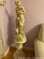 Side view of statue atop pedestal in room corner next to couch.