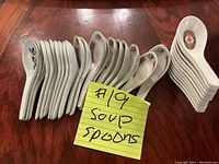 Top view showing 31 soup spoons separated into two groups: 20 ceramic spoons with floral designs stacked together and 11 white plastic spoons with an emblem design in a neat pile.