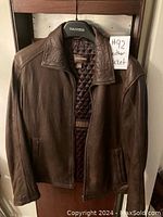 Front view of brown leather jacket on hanger showing quilted lining and Danier brand label