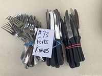 Photo of 24 forks and 24 knives bundled with rubber bands, placed on a white surface, including a handwritten note saying '#73 Forks Knives'