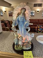 Front view of a 24-inch tall illuminated glass angel statue on a black circular base. The angel has flowing robes in blue and white, with a light halo of petals behind.