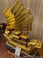 Front and side views of the gold dragon boat statue showing detailed dragon head, sails, and ornate architecture on a blue-green wave base.