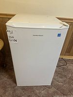 Front view of the white Hamilton Beach mini fridge showing some surface scuffs and a label on the door.