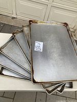 Eight large metal baking sheets stacked on top of each other showing size and condition, some discoloration and staining visible along edges