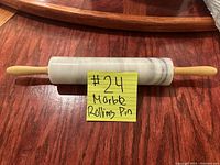 Full view of 18 inch marble rolling pin with light wooden handles on both ends, placed on wooden surface with a yellow note tagged '#24 Marbb Rolling Pin'.