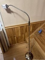 Full view of the metal adjustable floor lamp standing on wood floor against wall showing its height and structure