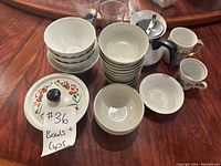 View showing stacked white bowls with floral designs, several cups, and the coffee pot with a label.