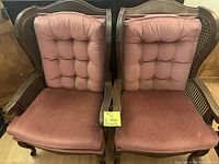 Pair of pink wooden framed armchairs with pink button-tufted backs and cane side panels, showing faded upholstery.