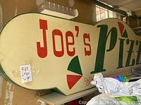Full view of vintage Joe's Pizza restaurant sign with distinct red and green lettering on a cream background.