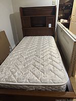 Full view of the bed frame with mattress showing the wood finish and mattress quilting.