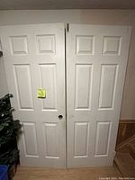 Photo showing pair of white double doors left and right with six recessed panels each, resting side by side on floor against wall.