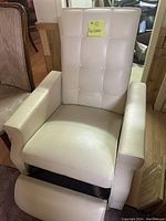 Photo of a white leather recliner chair showing tufted backrest, padded armrests, and extended footrest.