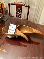 Two wooden bowls with long handled design placed on a glass table showing their smooth finish and natural wood grain.