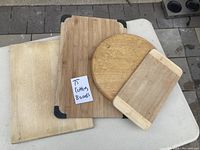Four wooden cutting boards set arranged on table. Boards include one large rounded rectangular with black corner protectors, a round board, a smaller rectangular board with rounded ends and one plain board.