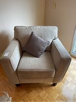 Front view of beige upholstered armchair with one square accent pillow