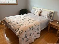 Full view of the bed setup showing cream-colored wooden bed frame and headboard, bedding with floral and light gray colors.