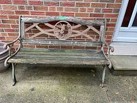 Full view of weathered outdoor bench with wooden slats and metal frame showing overall condition and dimensions placement outdoors near brick wall.