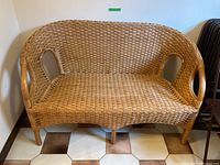 Front view of resin wicker bench showing two-seat design and curved armrests