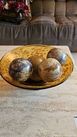 Top close-up view focusing on the glass bowl with four stone balls showing speckled amber coloring and marbled stone surfaces.