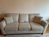 Front view of beige upholstered three-seat couch with two pillows