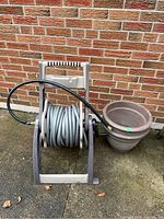 Hose Mobile hose reel with garden hose and two clay pots next to it outdoors on concrete floor against brick wall.