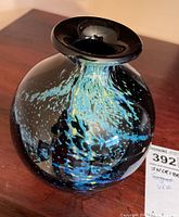Front and side views showing swirling blue and yellow patterns on black glass surface of the vase, with a wide flared mouth and rounded bulbous body.