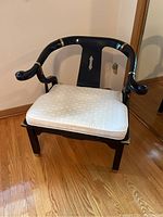 Front view of black lacquer armchair with white cushion and brass accents