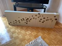 Large rectangular canvas painting with metallic flower designs laid against TV stand on parquet floor.