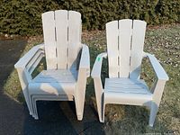 Two stacks of gray plastic Muskoka chairs outdoors on grass, showing their shape and color