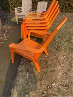 Side view of five stacked orange plastic Muskoka chairs outdoors on grass and sidewalk. Shows chair shape and stackability.