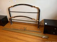 Overall view of dismantled bed frame components including headboard, footboard and side rails laid on hardwood floor