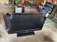 Samsung flat screen television angled showing screen and part of stand. Located in a garage area with miscellaneous items in background.