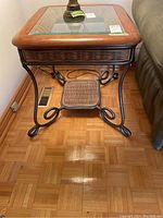 Front view showing metal frame with scrolled legs, wood and glass top, lower wicker shelf.
