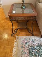 Photo of a square side table with metal frame, wood border around glass top, and wicker lower shelf on a wood parquet floor