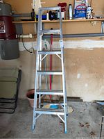 Full view of the six-foot aluminum step ladder standing fully open in a garage setting, showing structure and overall condition.