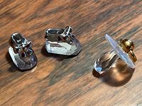Pair of clear faceted Swarovski crystal baby booties with silver metallic bows and a Swarovski crystal pacifier with a gold metallic ring placed on a wooden surface.