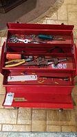 Top view of open red metal Flaherty tool box showing multiple compartments with assorted hand tools and hardware inside.