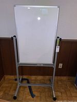 Front view of whiteboard on metal stand with caster wheels on tiled floor.