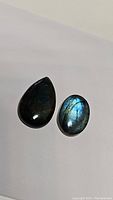 Two labradorite cabochons on a white background, showing dark base color with blue flash.